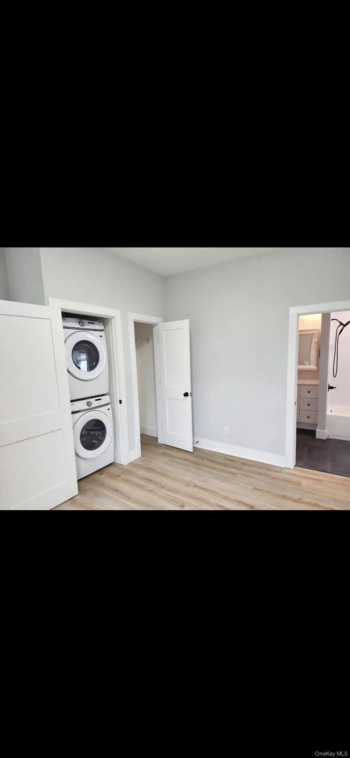 Laundry room featuring stacked washing machine and dryer and light wood-type flooring Laundry room featuring stacked washing machine and dryer and light wood-type flooring