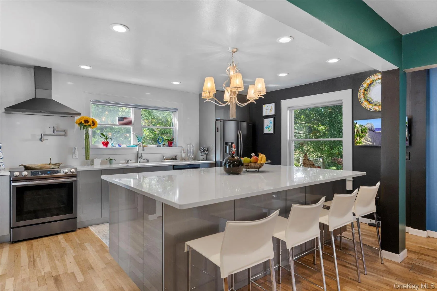Kitchen featuring stainless steel appliances, wall chimney range hood, light wood finished floors, a kitchen breakfast bar, and recessed lighting Kitchen featuring stainless steel appliances, wall chimney range hood, light wood finished floors, a kitchen breakfast bar, and recessed lighting