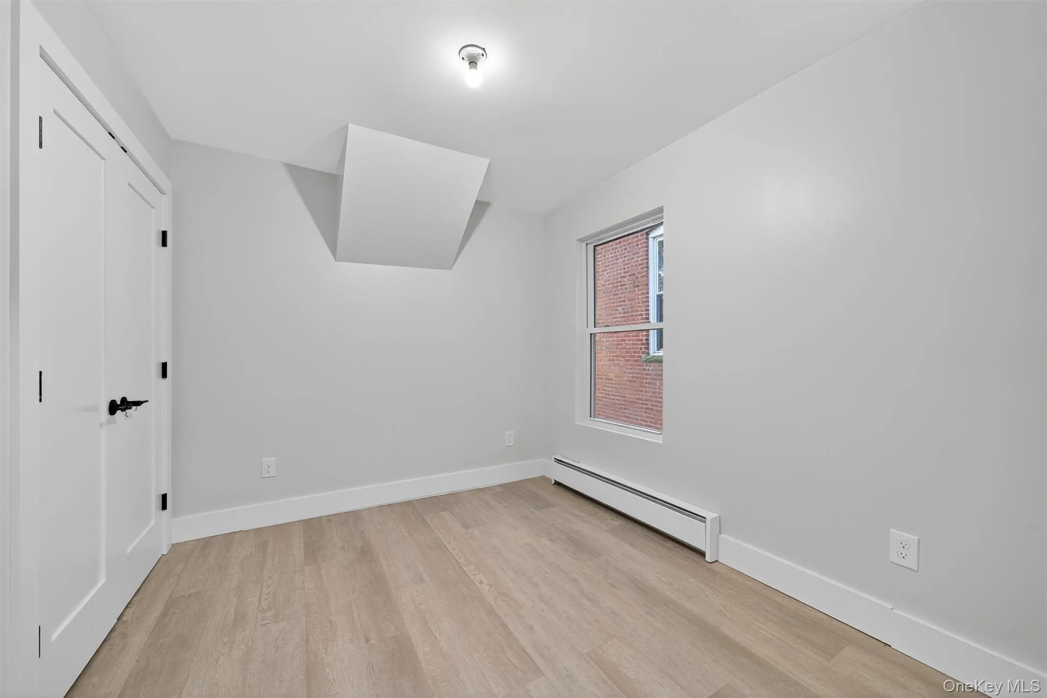Unfurnished bedroom featuring a baseboard radiator, light wood-style floors, and a closet Unfurnished bedroom featuring a baseboard radiator, light wood-style floors, and a closet