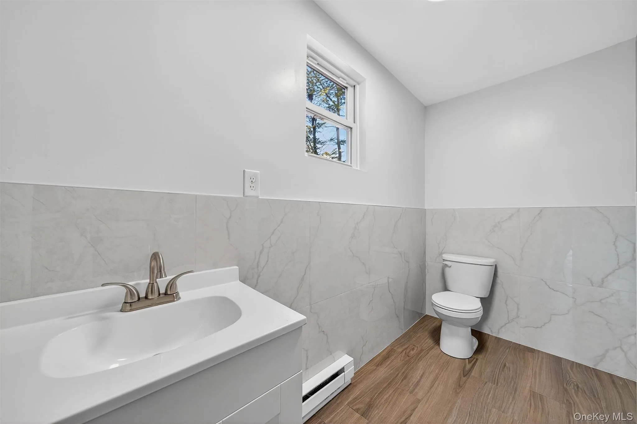 Half bath with vanity, baseboard heating, tile walls, wood finished floors, and a wainscoted wall Half bath with vanity, baseboard heating, tile walls, wood finished floors, and a wainscoted wall