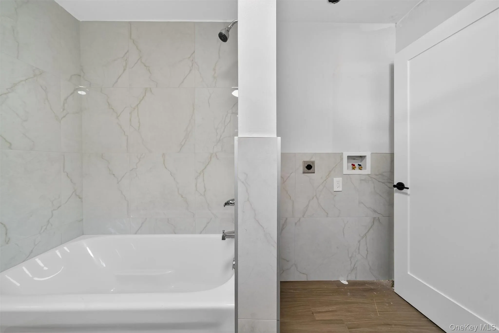 Bathroom featuring tile walls, a combined bath / shower with marble appearance, and wood finished floors Bathroom featuring tile walls, a combined bath / shower with marble appearance, and wood finished floors