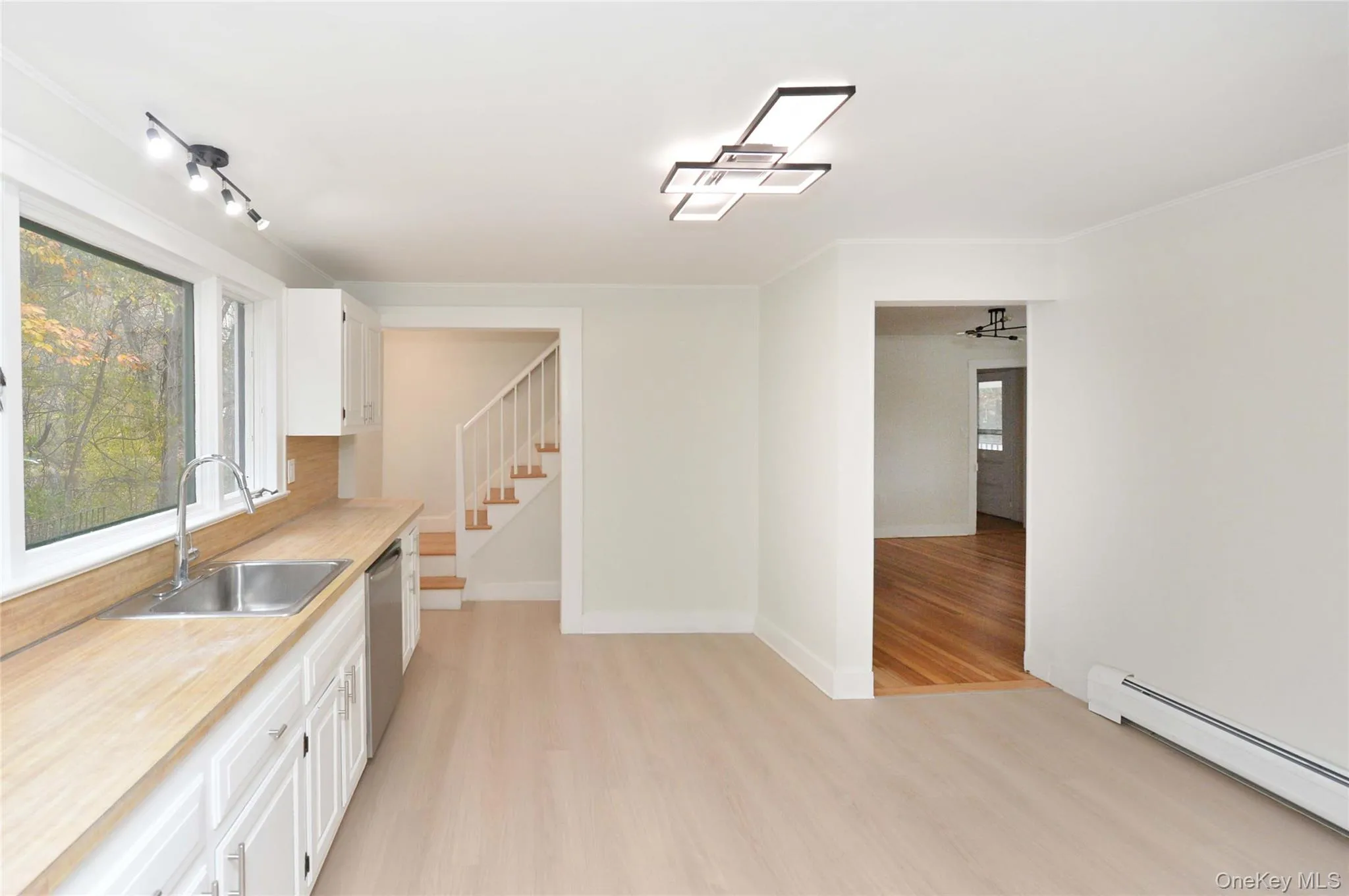 Kitchen with white cabinets, light countertops, light wood-type flooring, a baseboard radiator, and stainless steel dishwasher Kitchen with white cabinets, light countertops, light wood-type flooring, a baseboard radiator, and stainless steel dishwasher
