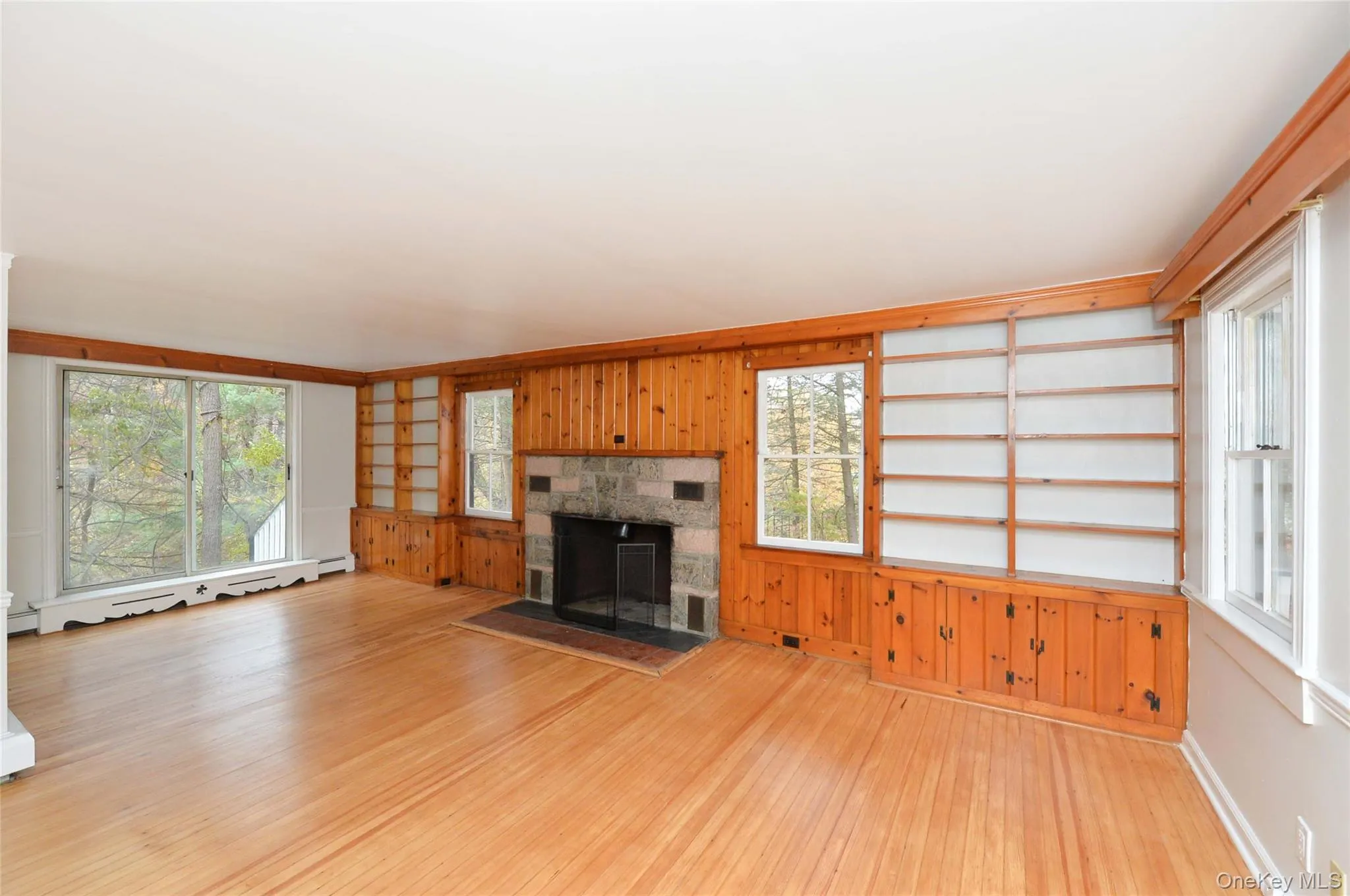 Unfurnished living room featuring wood walls, wood-type flooring, a fireplace, a baseboard radiator, and built in shelves Unfurnished living room featuring wood walls, wood-type flooring, a fireplace, a baseboard radiator, and built in shelves