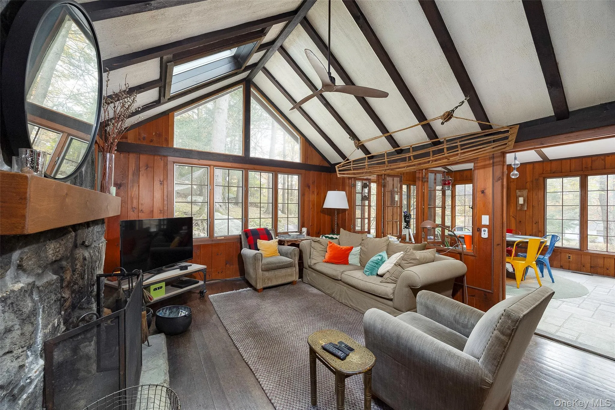 Living room featuring wooden walls, a skylight, a fireplace, beam ceiling, and wood finished floors Living room featuring wooden walls, a skylight, a fireplace, beam ceiling, and wood finished floors