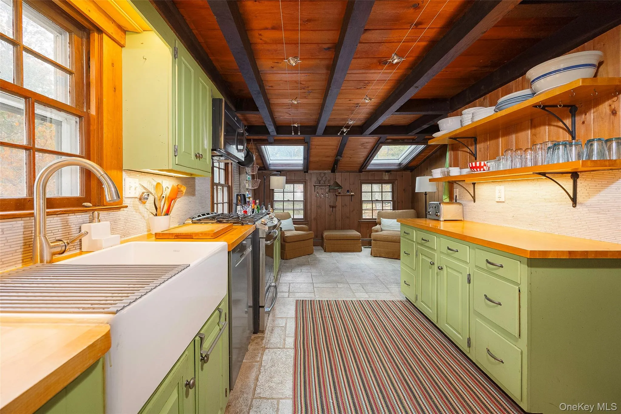 Kitchen with green cabinets, stainless steel appliances, open shelves, plenty of natural light, and a wooden ceiling with exposed beams Kitchen with green cabinets, stainless steel appliances, open shelves, plenty of natural light, and a wooden ceiling with exposed beams