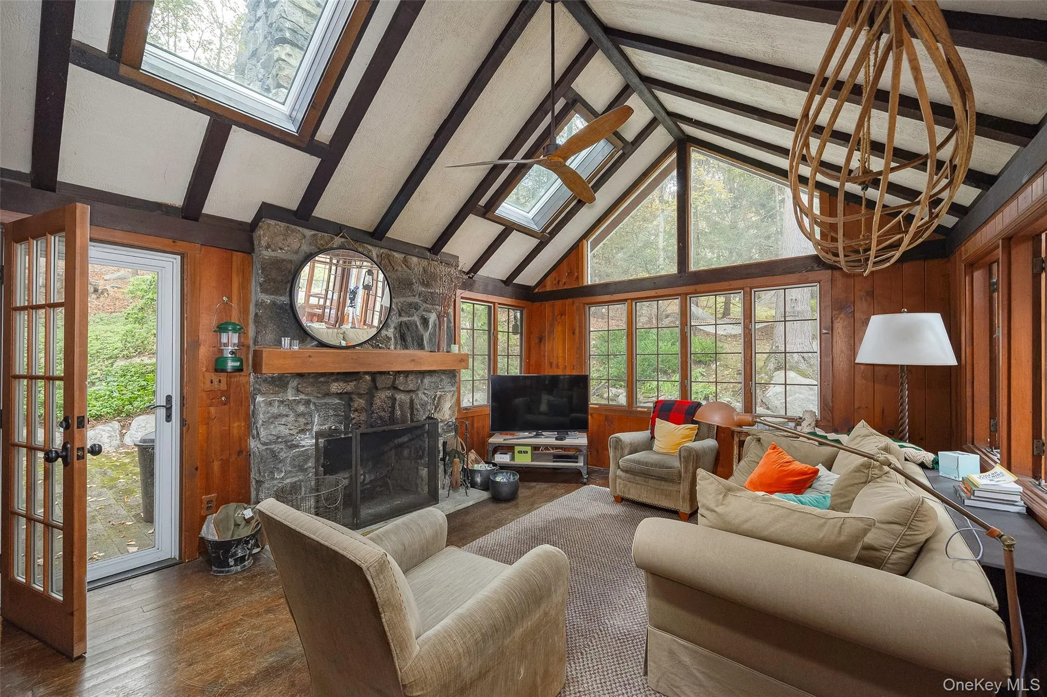 Living room featuring wooden walls, a skylight, a fireplace, beam ceiling, and wood finished floors Living room featuring wooden walls, a skylight, a fireplace, beam ceiling, and wood finished floors