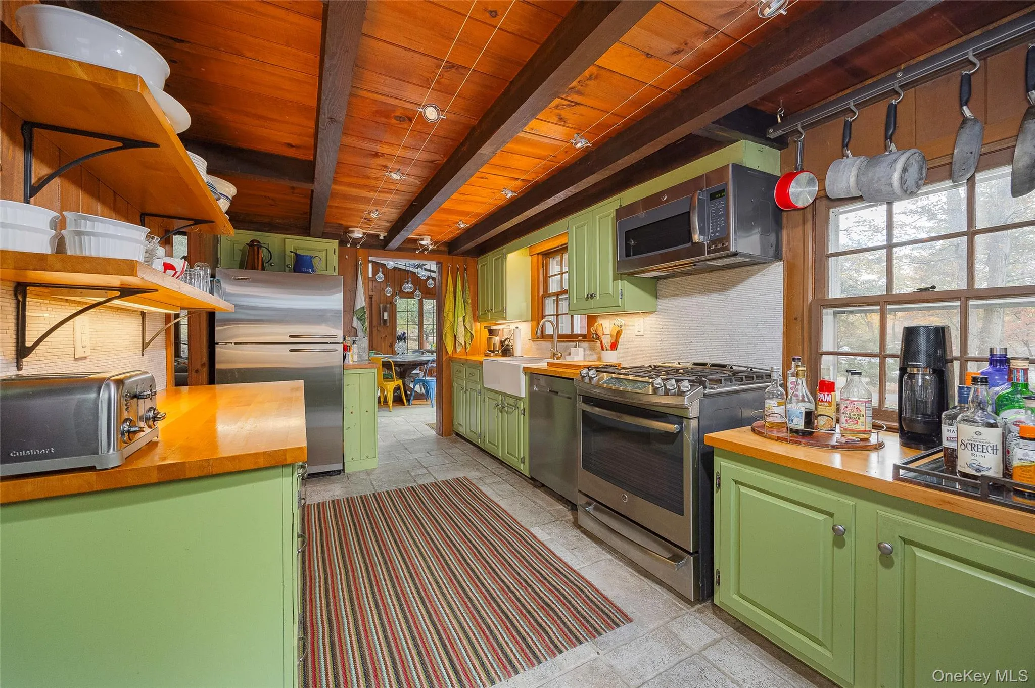 Kitchen with green cabinets, stainless steel appliances, open shelves, plenty of natural light, and a wooden ceiling with exposed beams Kitchen with green cabinets, stainless steel appliances, open shelves, plenty of natural light, and a wooden ceiling with exposed beams