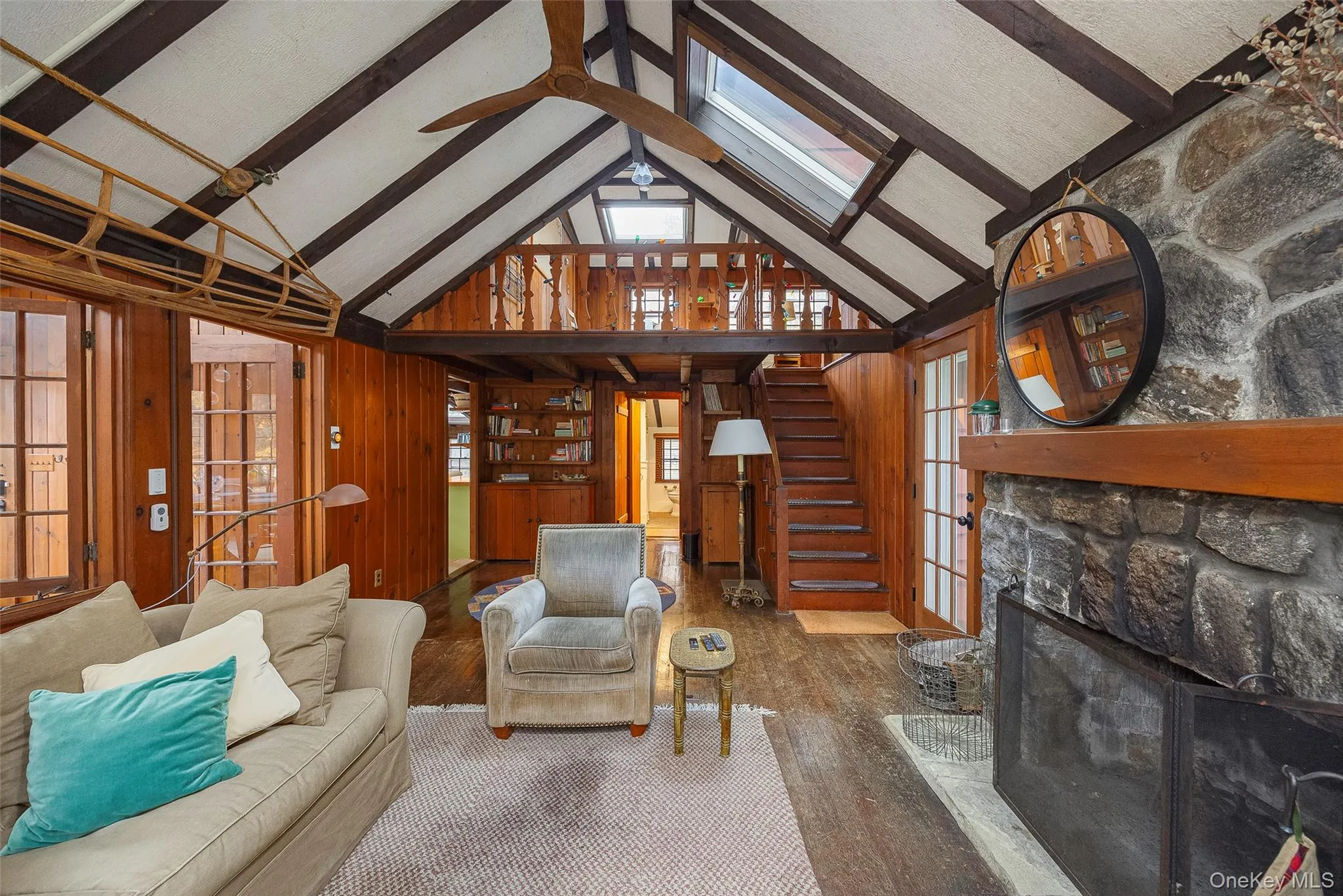 Living room featuring wooden walls, a skylight, a fireplace, beam ceiling, and wood finished floors Living room featuring wooden walls, a skylight, a fireplace, beam ceiling, and wood finished floors