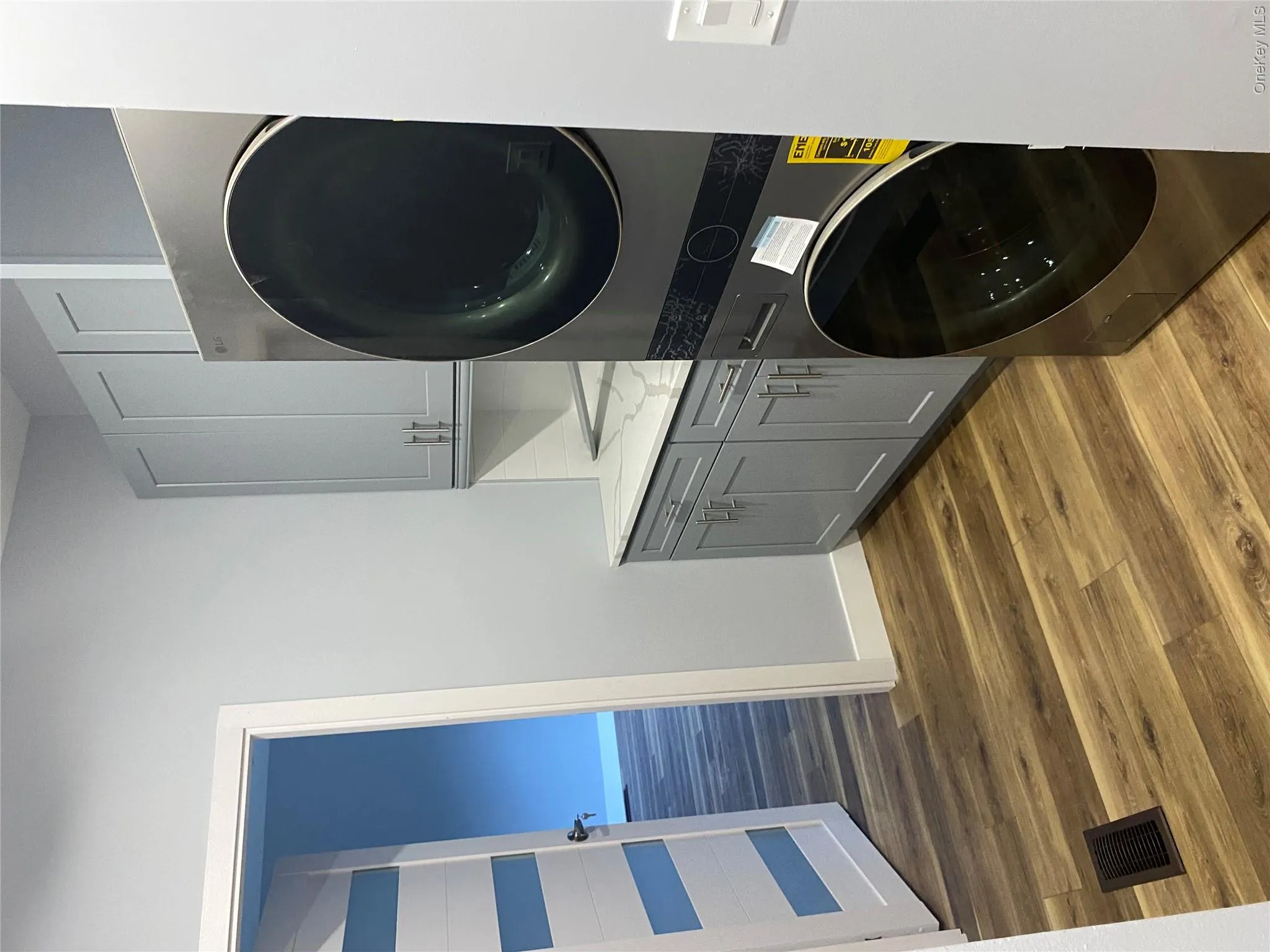 Washroom with dark wood-style flooring, stacked washer and clothes dryer, and cabinet space Washroom with dark wood-style flooring, stacked washer and clothes dryer, and cabinet space