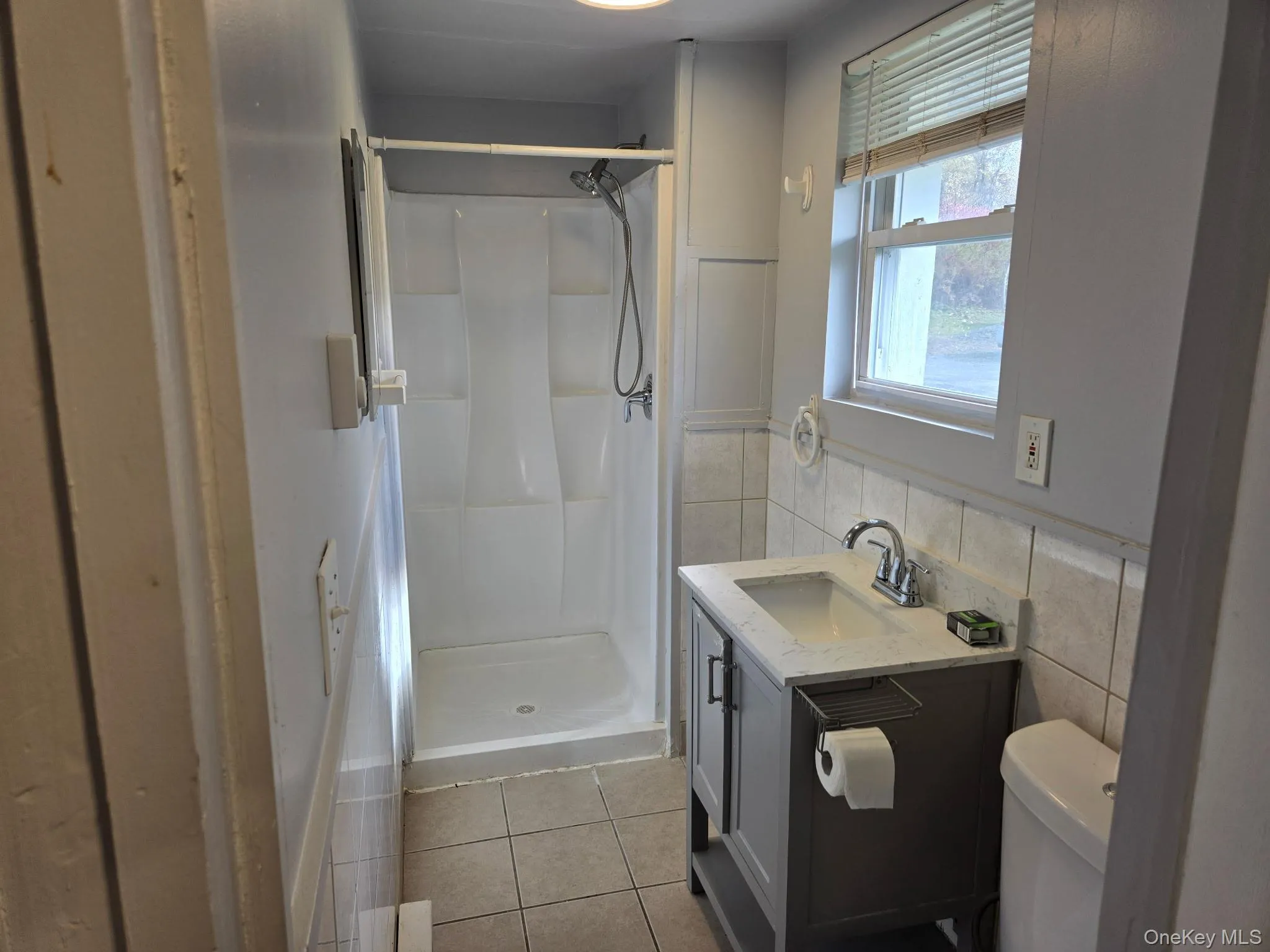 Full bathroom featuring light tile patterned flooring, a stall shower, vanity, and tile walls Full bathroom featuring light tile patterned flooring, a stall shower, vanity, and tile walls