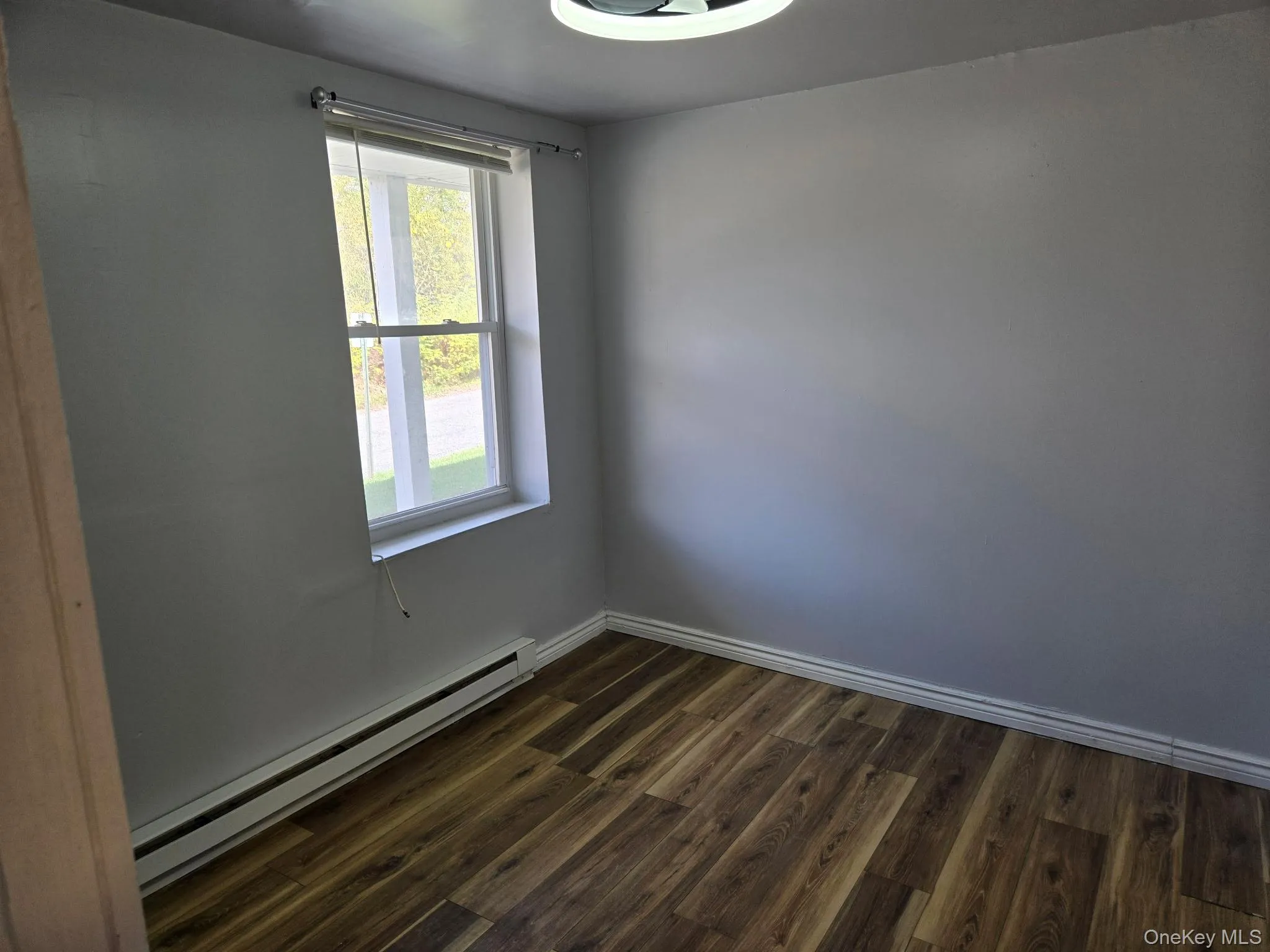 Empty room featuring a baseboard heating unit and dark wood-style floors Empty room featuring a baseboard heating unit and dark wood-style floors