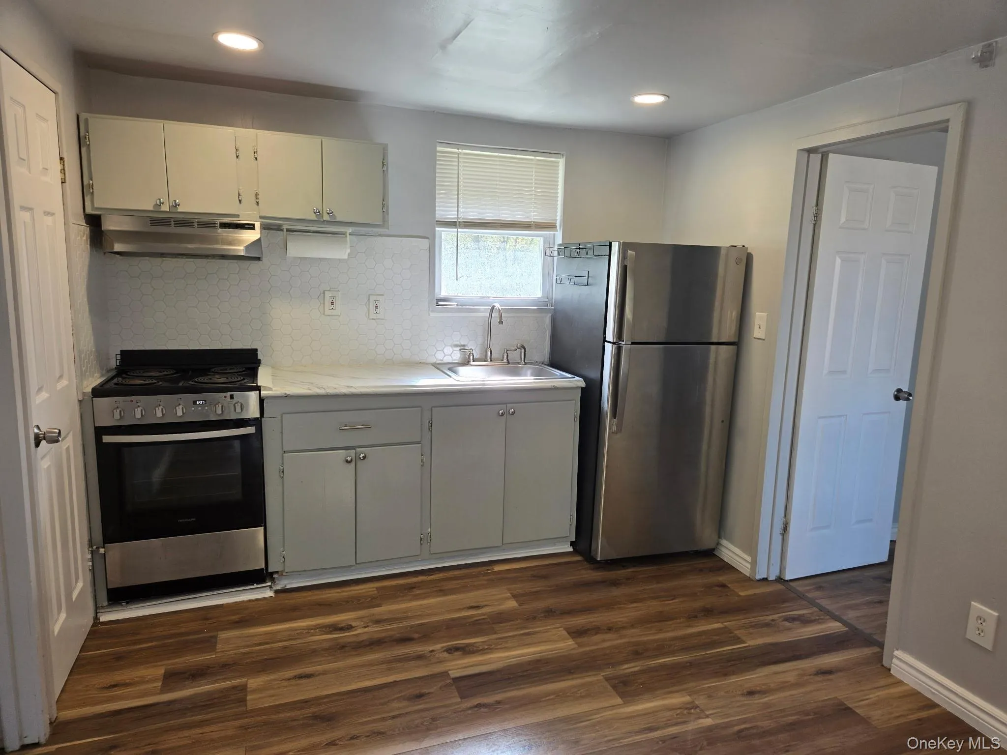 Kitchen featuring stainless steel appliances, backsplash, light countertops, under cabinet range hood, and dark wood-style floors Kitchen featuring stainless steel appliances, backsplash, light countertops, under cabinet range hood, and dark wood-style floors