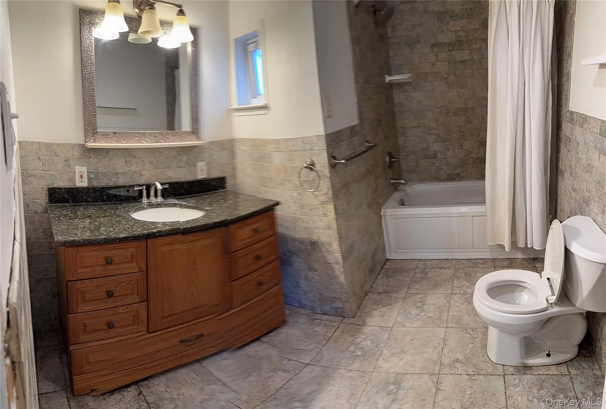 Bathroom featuring tile walls, a wainscoted wall, shower / tub combo with curtain, and vanity Bathroom featuring tile walls, a wainscoted wall, shower / tub combo with curtain, and vanity