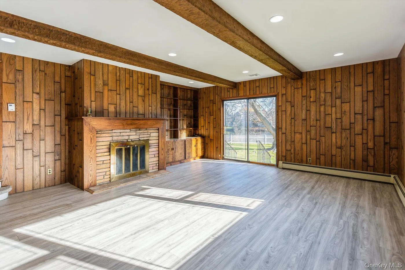 Unfurnished living room featuring wood walls, beam ceiling, a stone fireplace, recessed lighting, and wood finished floors Unfurnished living room featuring wood walls, beam ceiling, a stone fireplace, recessed lighting, and wood finished floors