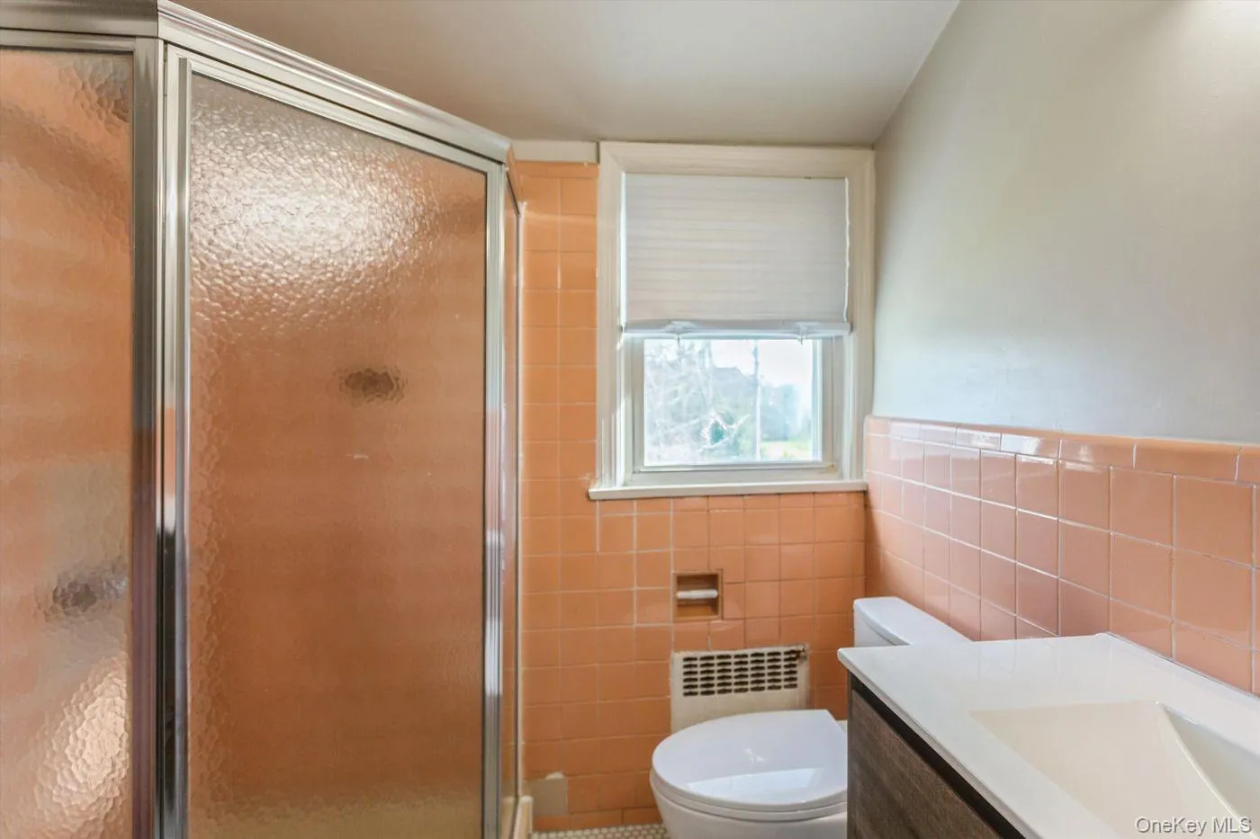 Bathroom featuring a stall shower, vanity, radiator, a wainscoted wall, and tile walls Bathroom featuring a stall shower, vanity, radiator, a wainscoted wall, and tile walls