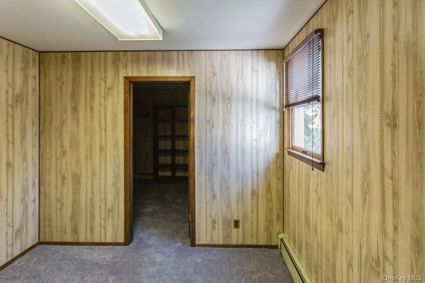 Unfurnished room with wooden walls, a baseboard radiator, and dark carpet Unfurnished room with wooden walls, a baseboard radiator, and dark carpet