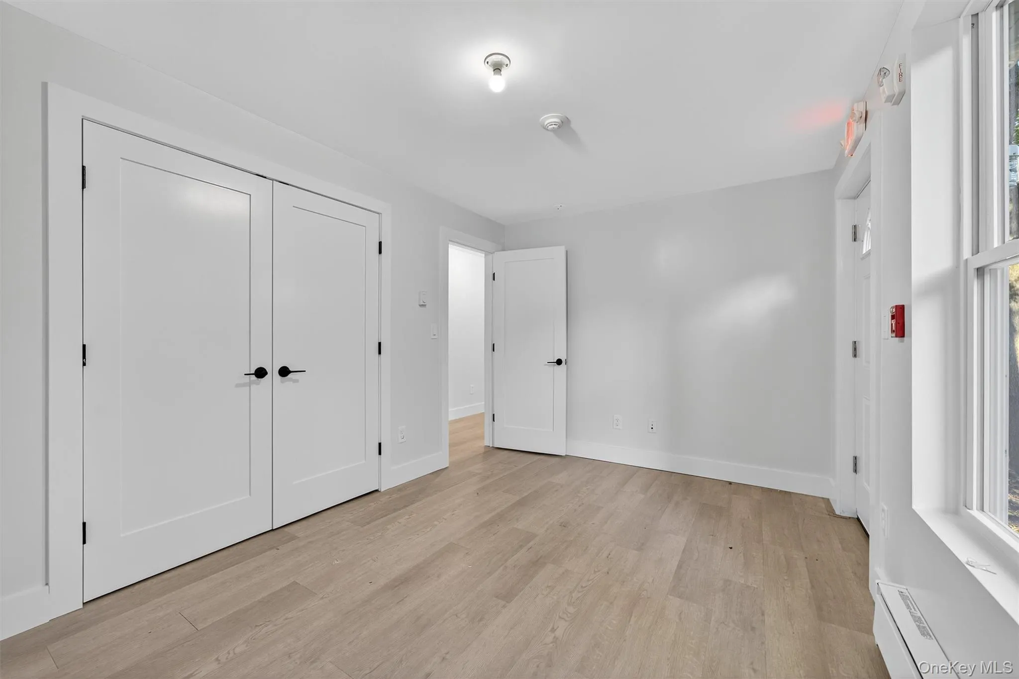 Unfurnished bedroom with a baseboard radiator, light wood-type flooring, and a closet Unfurnished bedroom with a baseboard radiator, light wood-type flooring, and a closet