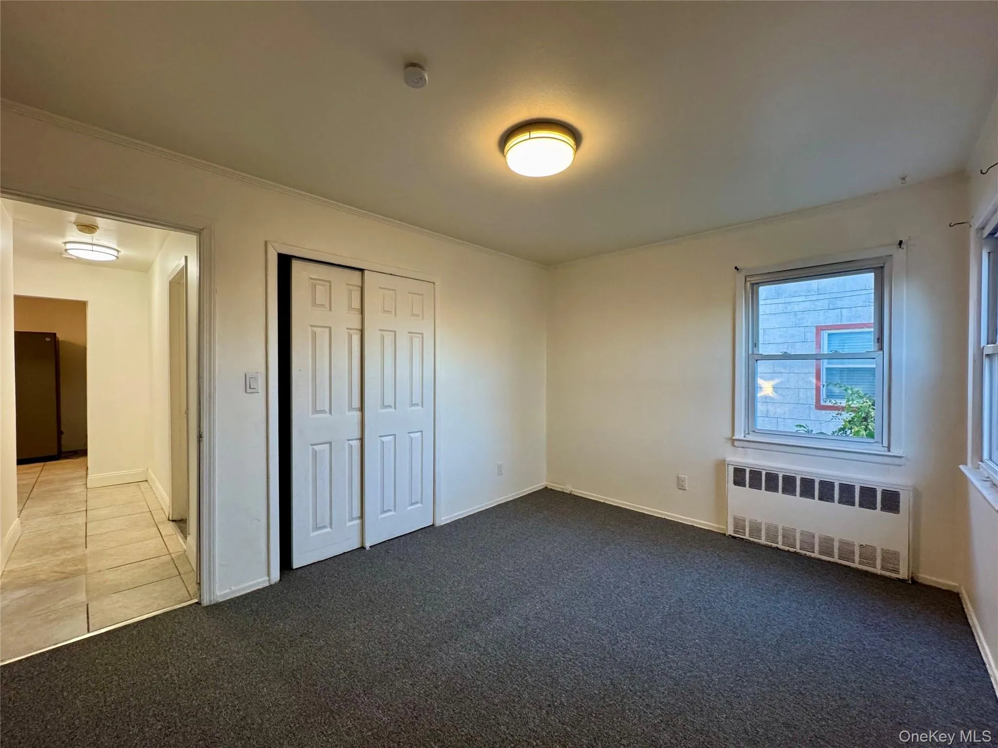 Unfurnished bedroom with radiator, carpet floors, a closet, crown molding, and tile patterned flooring Unfurnished bedroom with radiator, carpet floors, a closet, crown molding, and tile patterned flooring