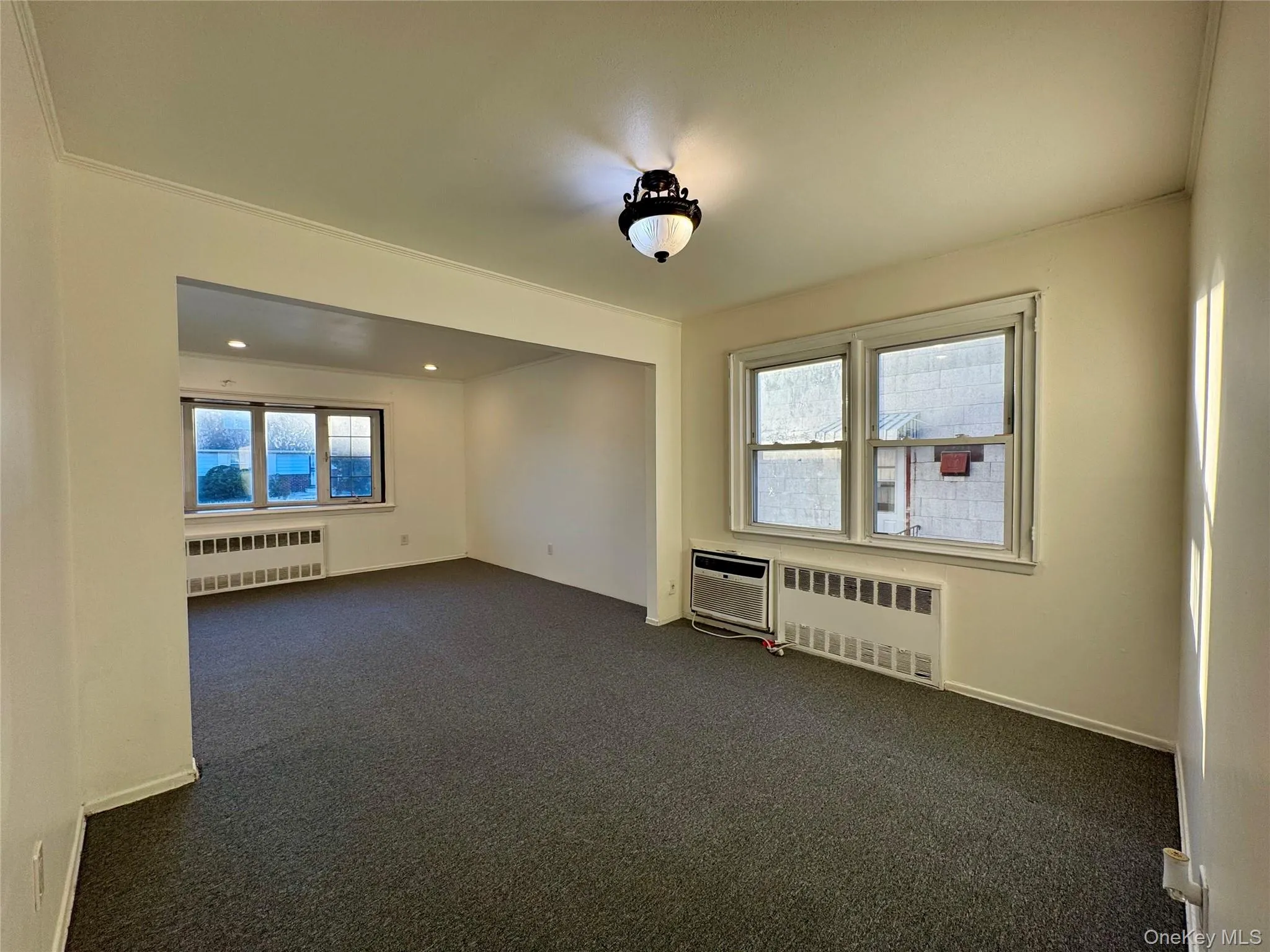 Spare room featuring dark carpet, radiator heating unit, crown molding, and an AC wall unit Spare room featuring dark carpet, radiator heating unit, crown molding, and an AC wall unit