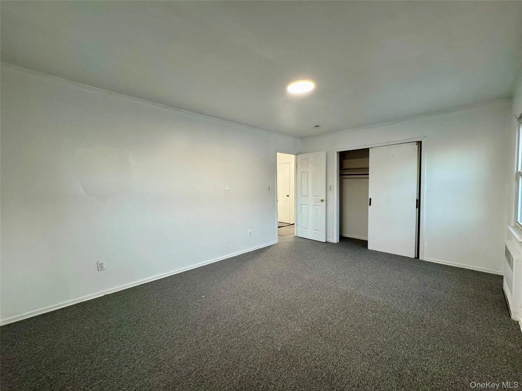 Unfurnished bedroom featuring dark colored carpet, a closet, and radiator heating unit Unfurnished bedroom featuring dark colored carpet, a closet, and radiator heating unit