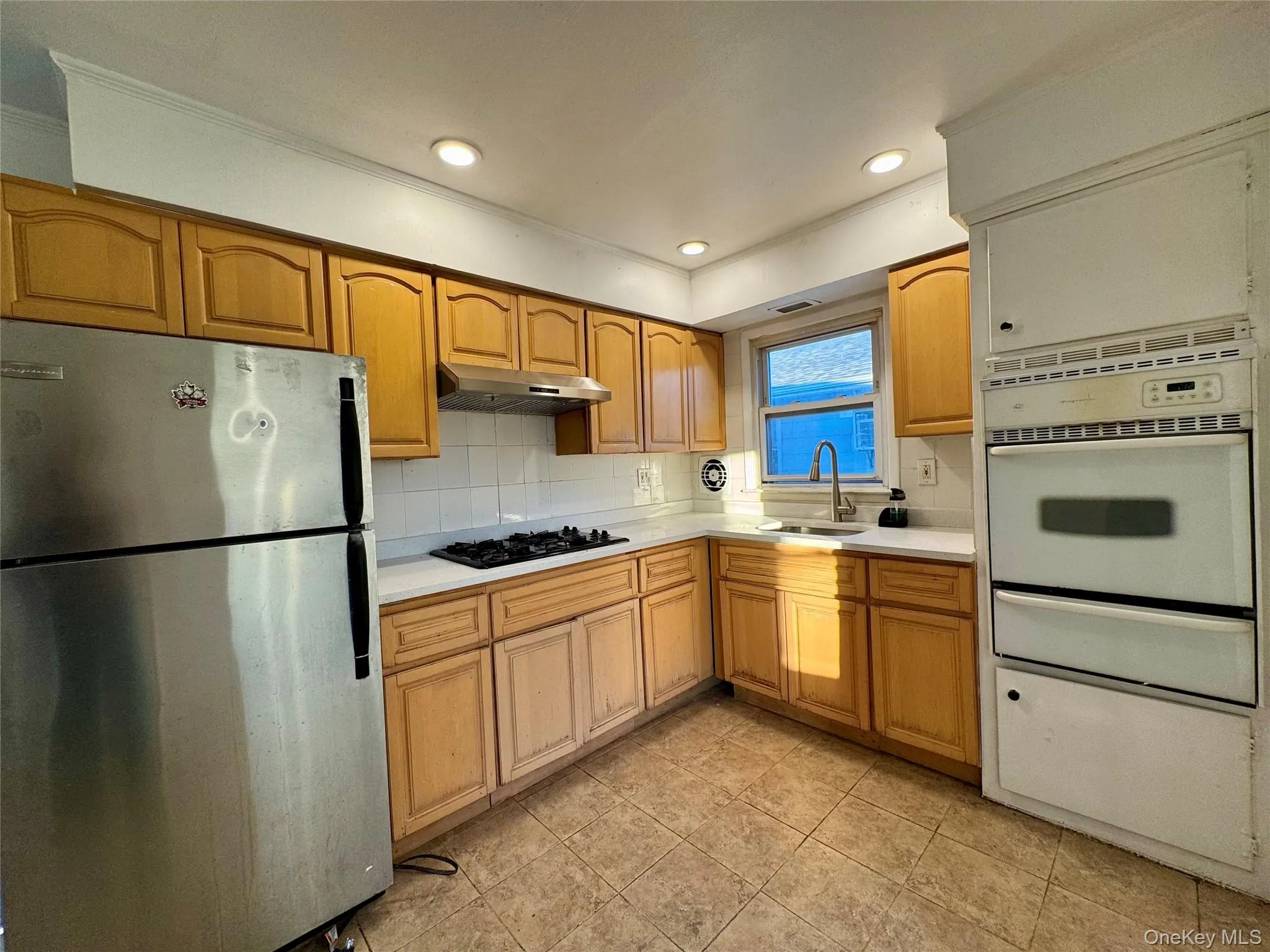 Kitchen featuring freestanding refrigerator, light countertops, oven, tasteful backsplash, and a warming drawer Kitchen featuring freestanding refrigerator, light countertops, oven, tasteful backsplash, and a warming drawer