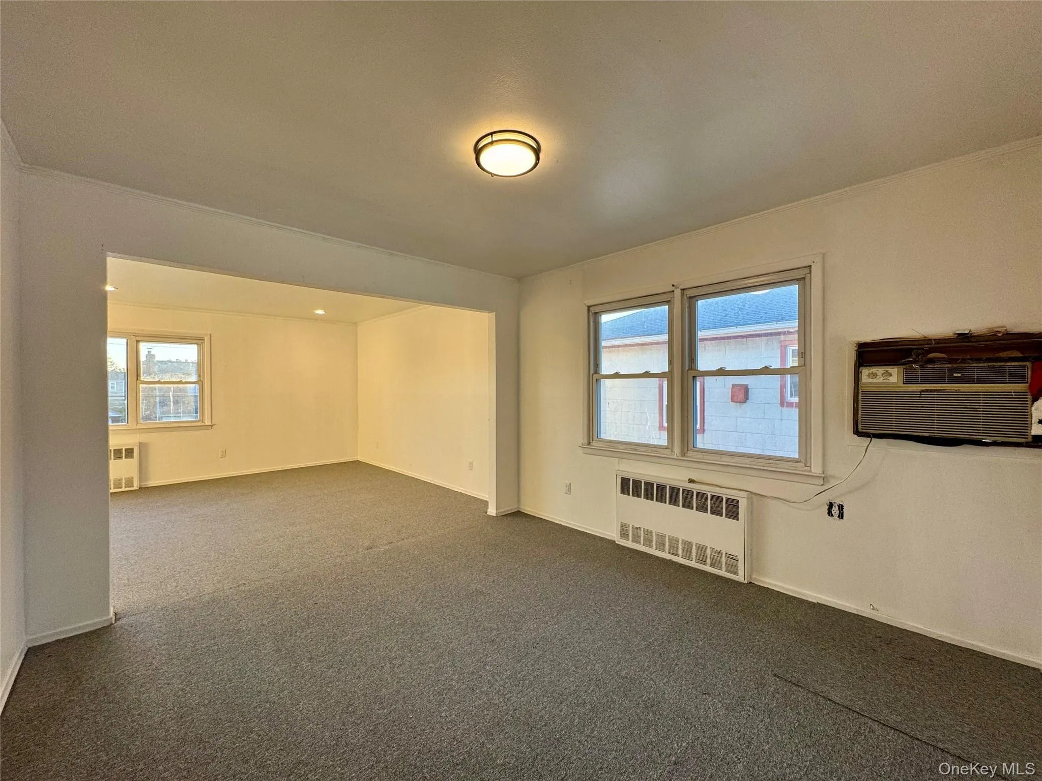 Carpeted empty room with radiator and a wall unit AC Carpeted empty room with radiator and a wall unit AC