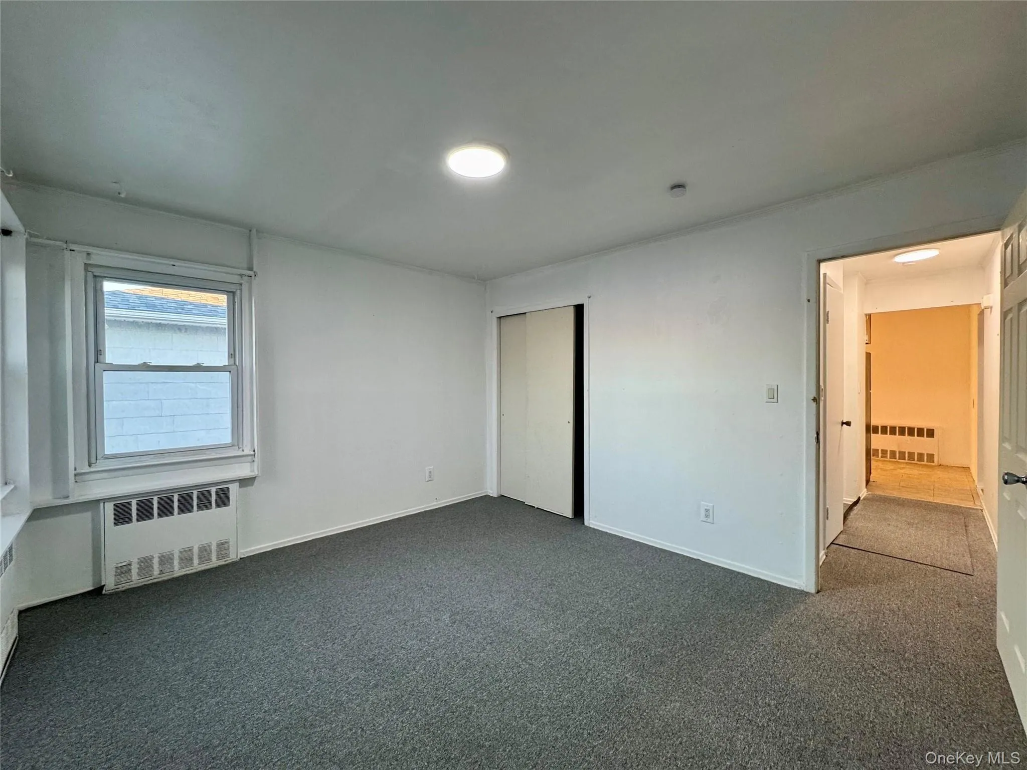 Unfurnished bedroom with radiator, carpet flooring, and a closet Unfurnished bedroom with radiator, carpet flooring, and a closet