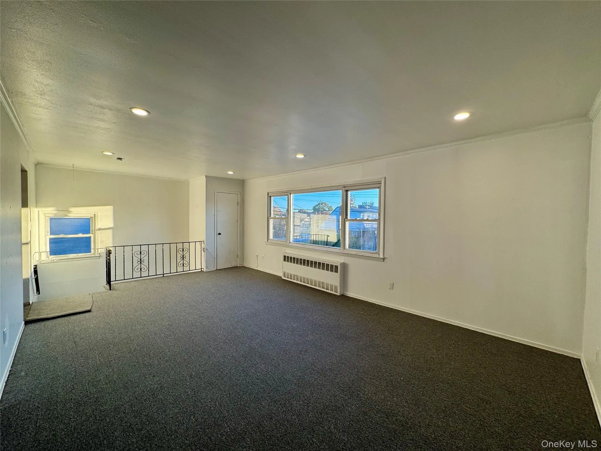 Carpeted empty room featuring radiator heating unit, recessed lighting, and vaulted ceiling Carpeted empty room featuring radiator heating unit, recessed lighting, and vaulted ceiling