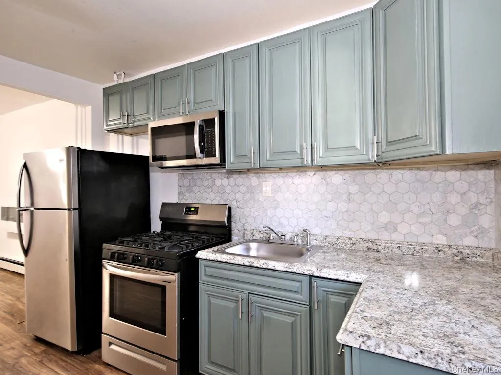 Kitchen featuring appliances with stainless steel finishes, backsplash, light countertops, gray cabinetry, and dark wood-type flooring Kitchen featuring appliances with stainless steel finishes, backsplash, light countertops, gray cabinetry, and dark wood-type flooring