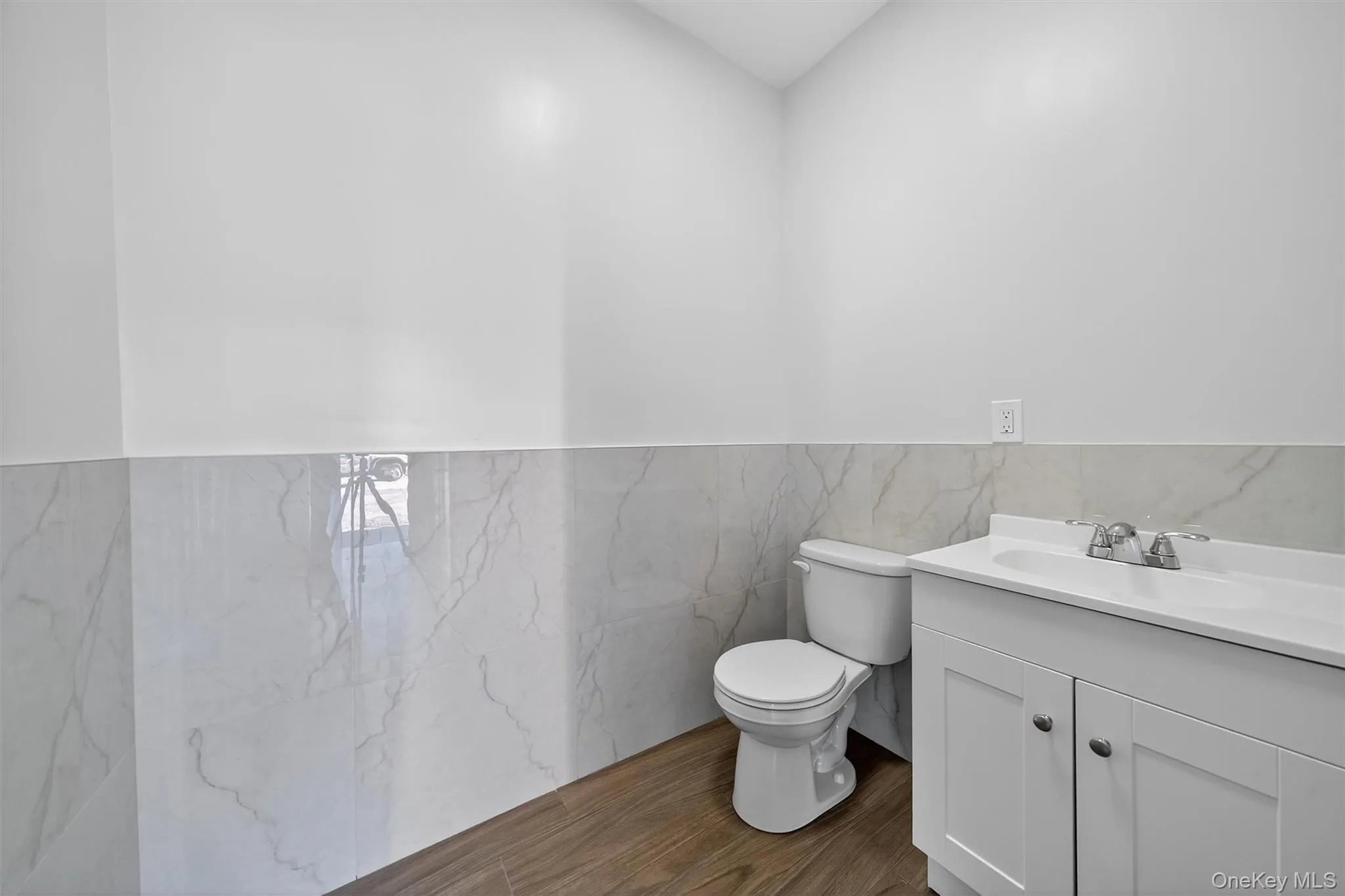 Half bathroom with tile walls, vanity, dark wood finished floors, and wainscoting Half bathroom with tile walls, vanity, dark wood finished floors, and wainscoting