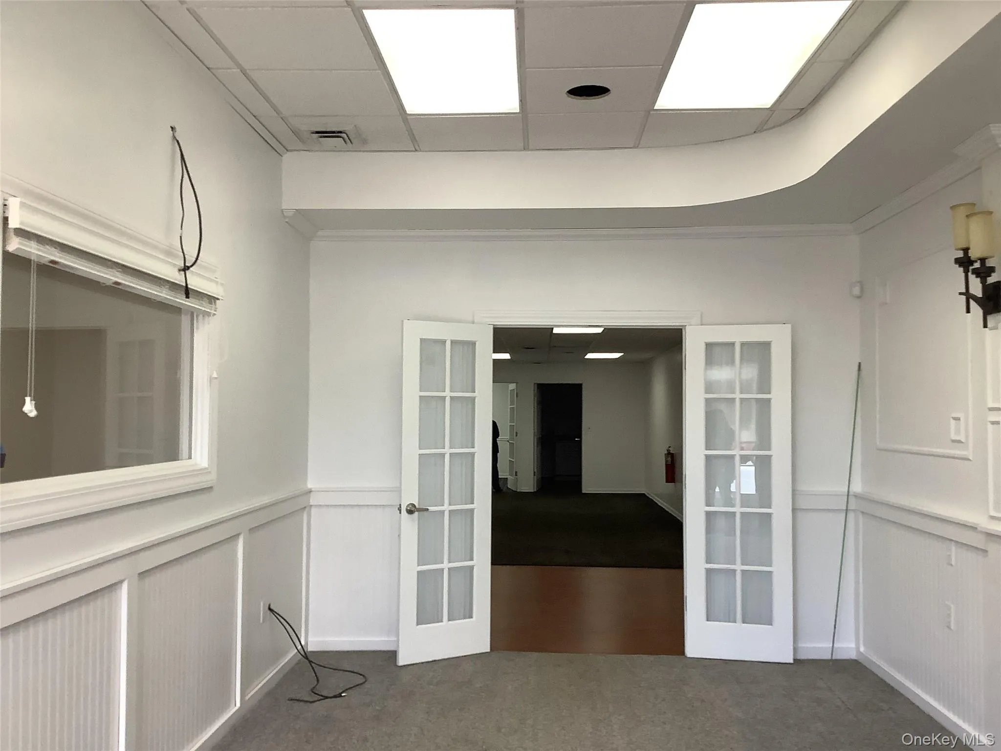 Empty room with french doors, carpet, a drop ceiling, and a wainscoted wall Empty room with french doors, carpet, a drop ceiling, and a wainscoted wall