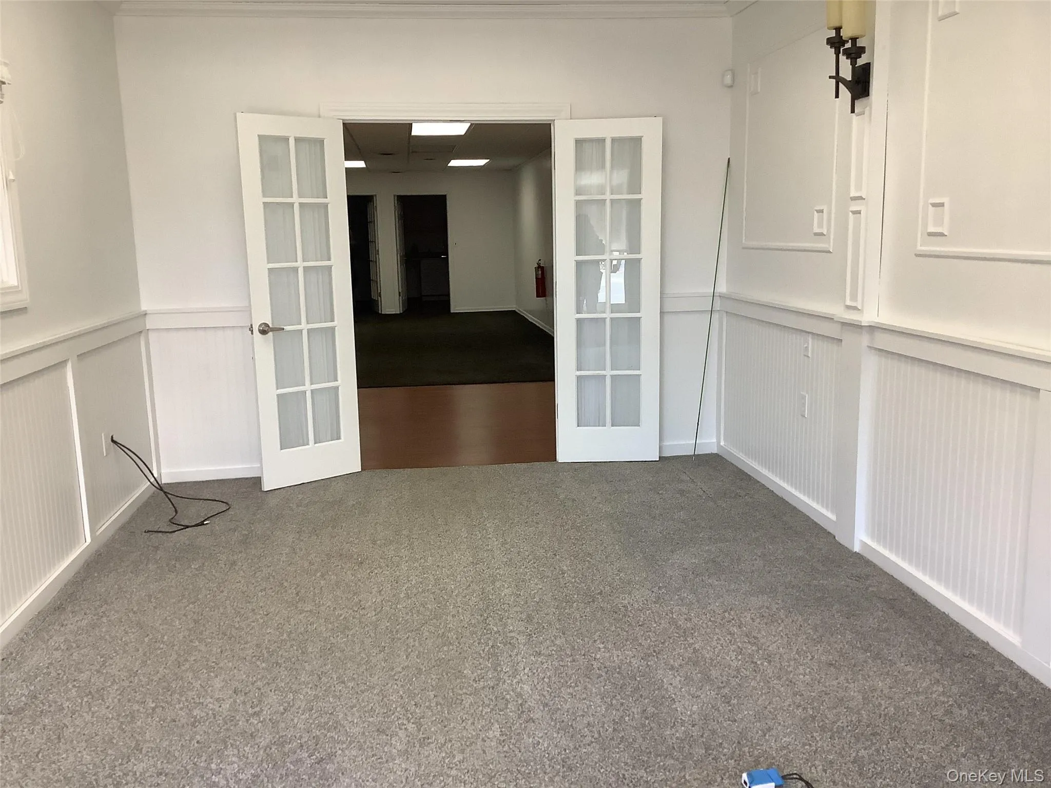 Unfurnished dining area with french doors, carpet floors, wainscoting, and a decorative wall Unfurnished dining area with french doors, carpet floors, wainscoting, and a decorative wall