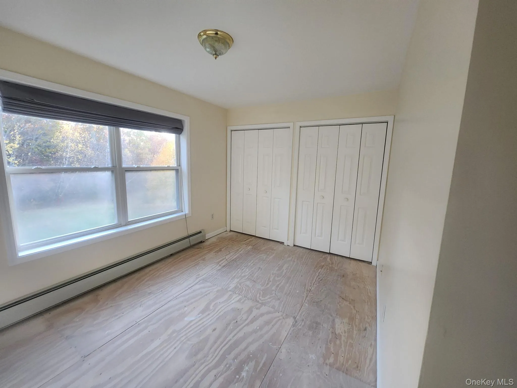 Unfurnished 2nd bedroom featuring two closets and a baseboard heating unit. Unfurnished 2nd bedroom featuring two closets and a baseboard heating unit.