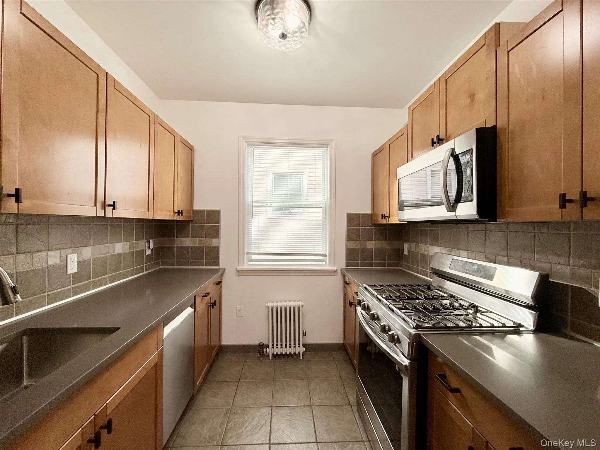 Kitchen with stainless steel appliances, dark countertops, light tile patterned floors, and brown cabinets Kitchen with stainless steel appliances, dark countertops, light tile patterned floors, and brown cabinets