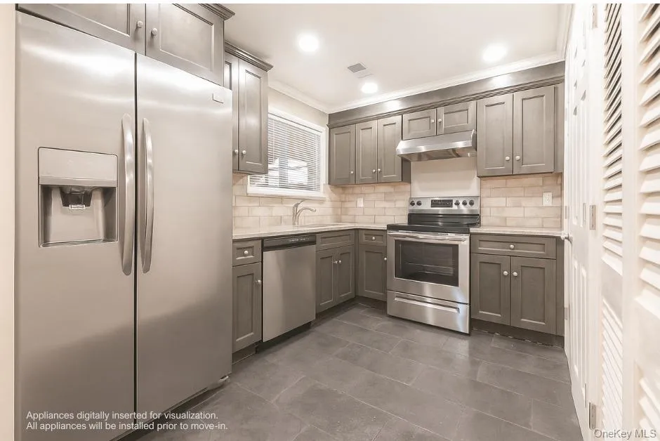 Kitchen featuring appliances with stainless steel finishes, decorative backsplash, ornamental molding, under cabinet range hood, and light stone countertops Kitchen featuring appliances with stainless steel finishes, decorative backsplash, ornamental molding, under cabinet range hood, and light stone countertops
