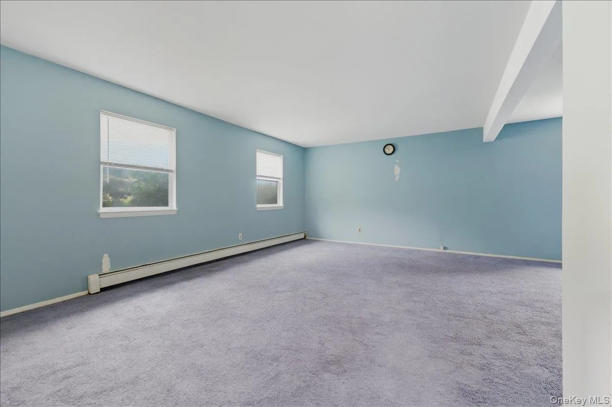 Carpeted empty room with baseboard heating and beamed ceiling Carpeted empty room with baseboard heating and beamed ceiling
