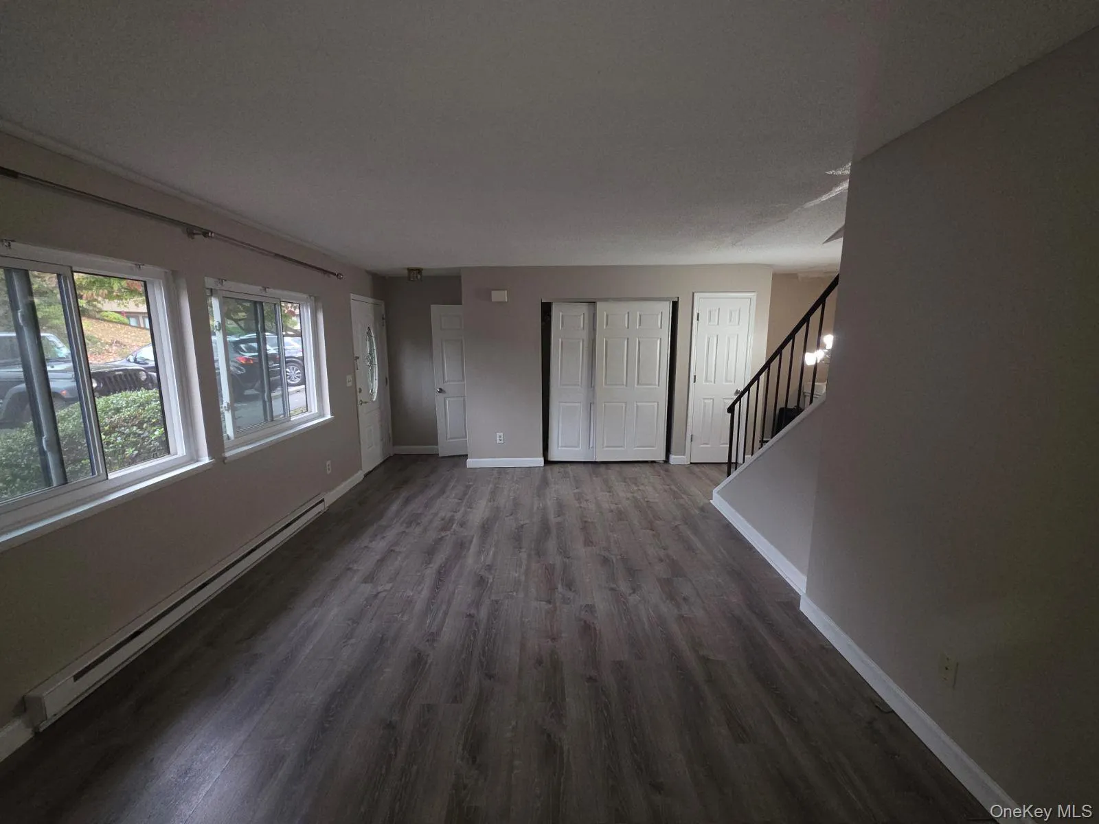 Unfurnished living room with a baseboard heating unit, stairway, and dark wood-type flooring Unfurnished living room with a baseboard heating unit, stairway, and dark wood-type flooring