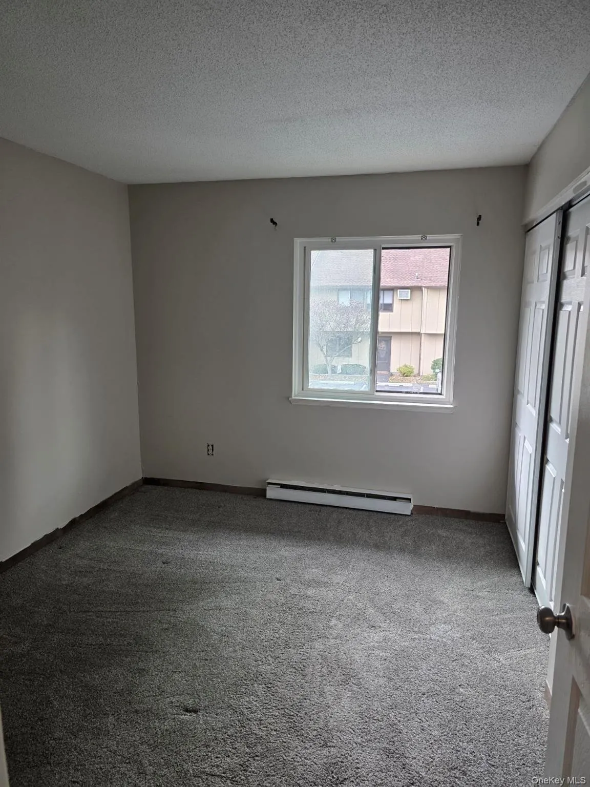 Unfurnished bedroom with a textured ceiling, carpet, a closet, and a baseboard radiator Unfurnished bedroom with a textured ceiling, carpet, a closet, and a baseboard radiator
