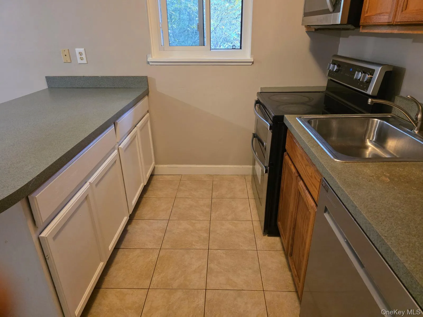 Kitchen with dark countertops, appliances with stainless steel finishes, and light tile patterned floors Kitchen with dark countertops, appliances with stainless steel finishes, and light tile patterned floors