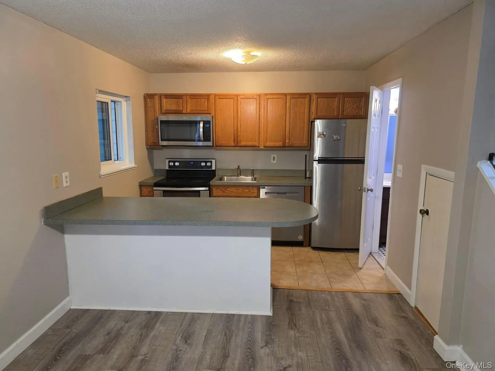 Kitchen with stainless steel appliances, brown cabinetry, a textured ceiling, a peninsula, and light wood finished floors Kitchen with stainless steel appliances, brown cabinetry, a textured ceiling, a peninsula, and light wood finished floors