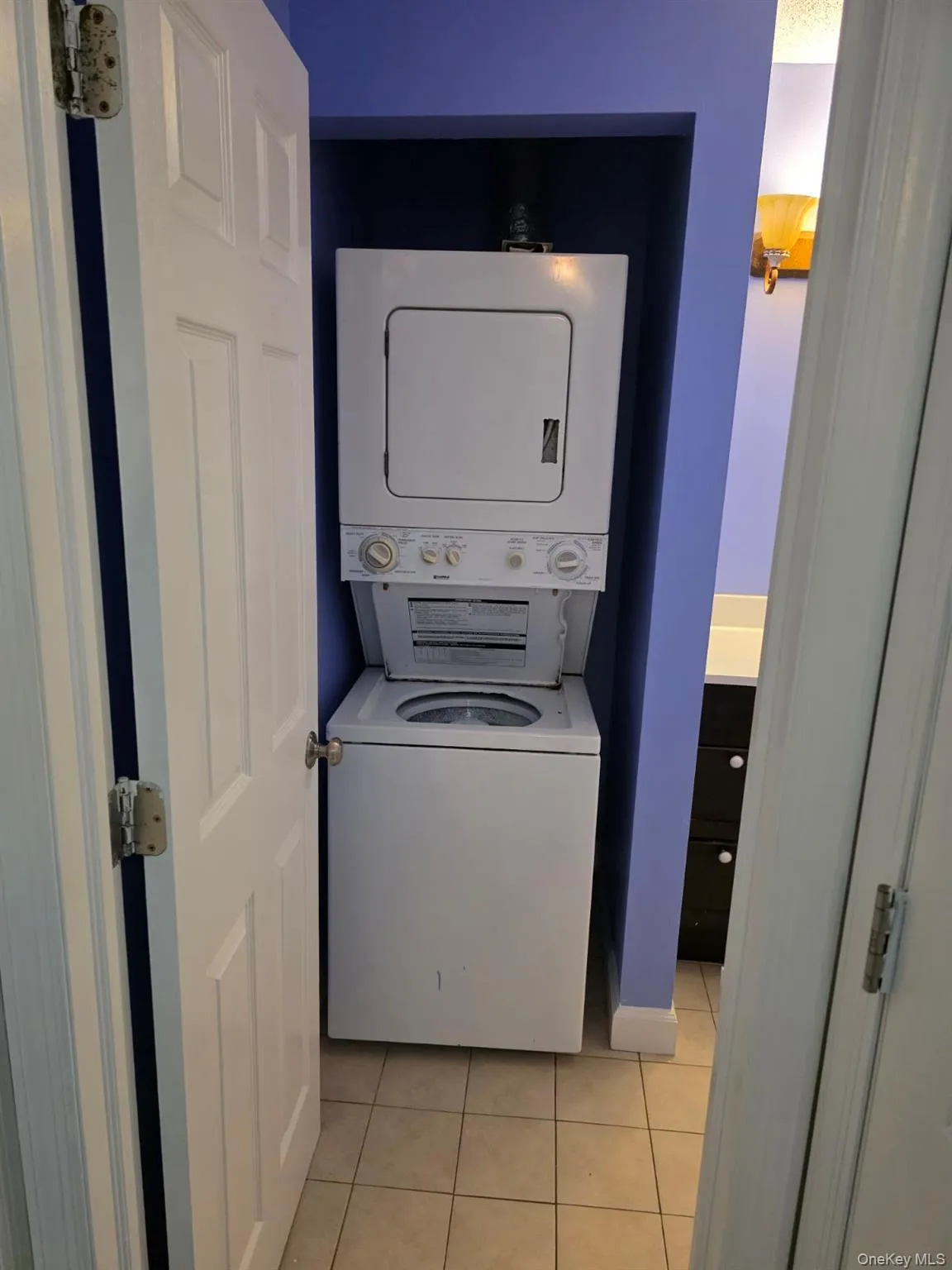 Washroom featuring light tile patterned flooring and stacked washer / drying machine Washroom featuring light tile patterned flooring and stacked washer / drying machine