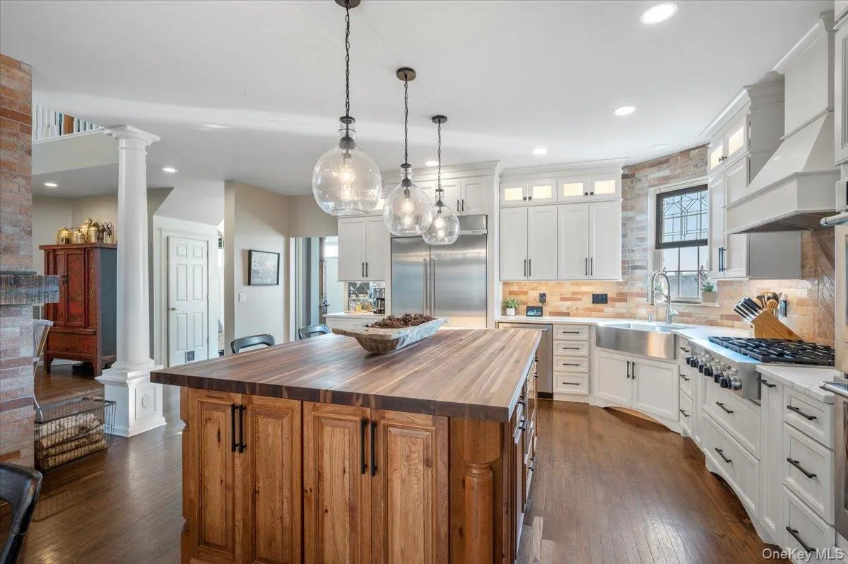 Kitchen featuring butcher block counters, a center island, glass insert cabinets, hanging light fixtures, and stainless steel appliances Kitchen featuring butcher block counters, a center island, glass insert cabinets, hanging light fixtures, and stainless steel appliances