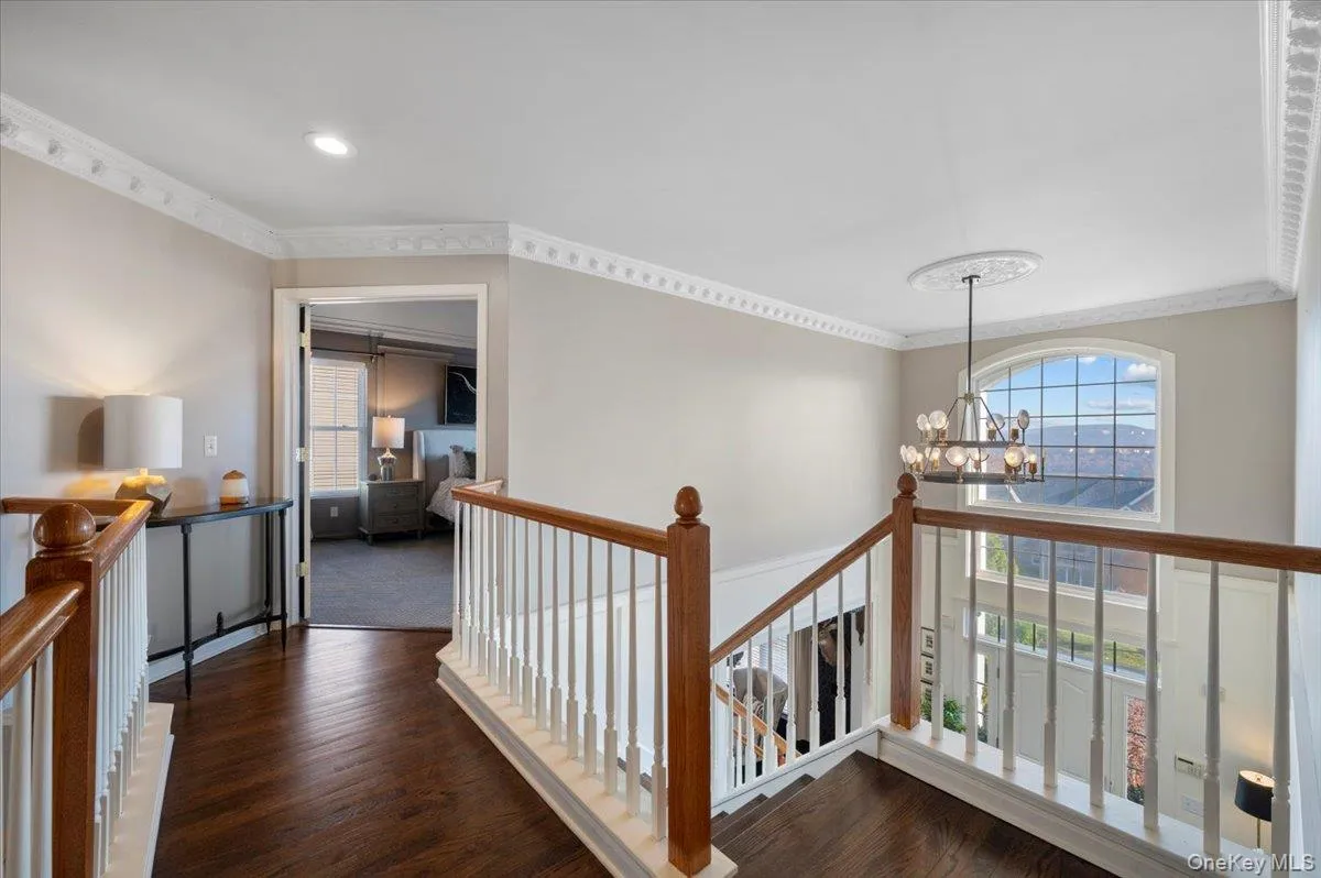 Corridor featuring an upstairs landing, dark wood-style flooring, ornamental molding, and a chandelier Corridor featuring an upstairs landing, dark wood-style flooring, ornamental molding, and a chandelier