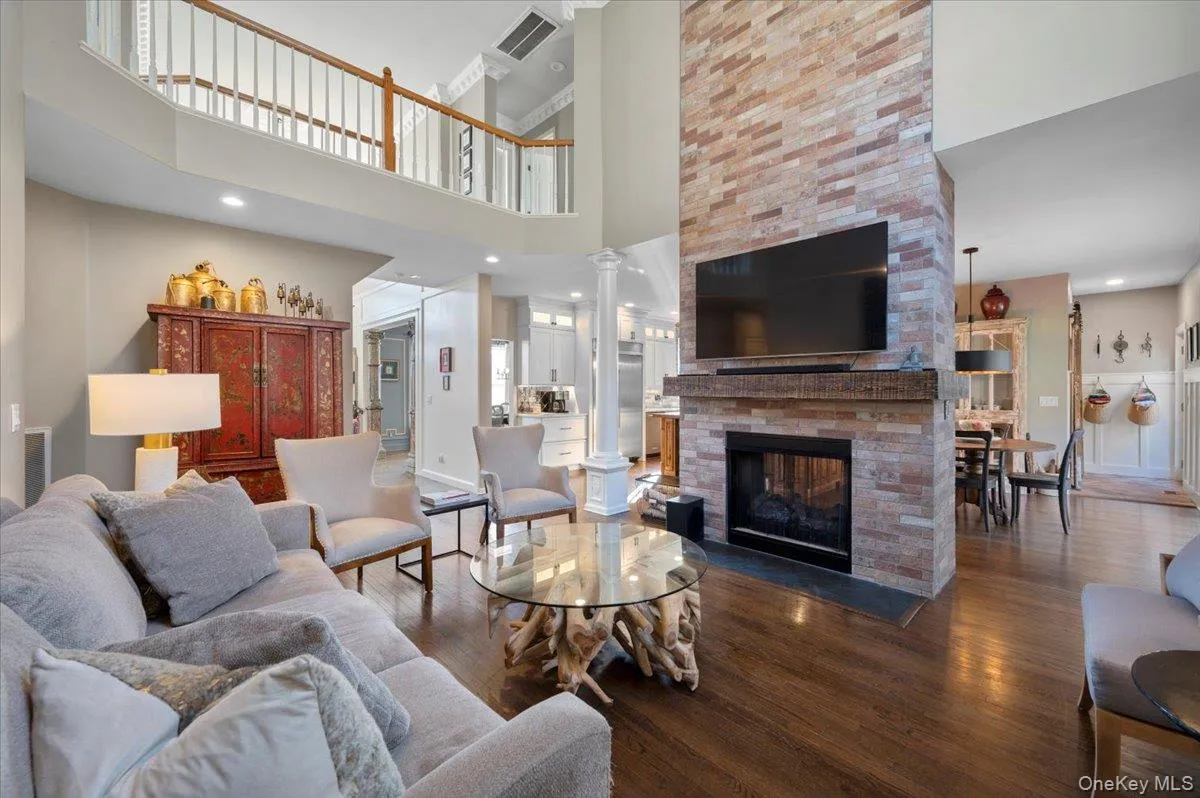 Living room featuring wood finished floors, a large fireplace, a high ceiling, recessed lighting, and decorative columns Living room featuring wood finished floors, a large fireplace, a high ceiling, recessed lighting, and decorative columns