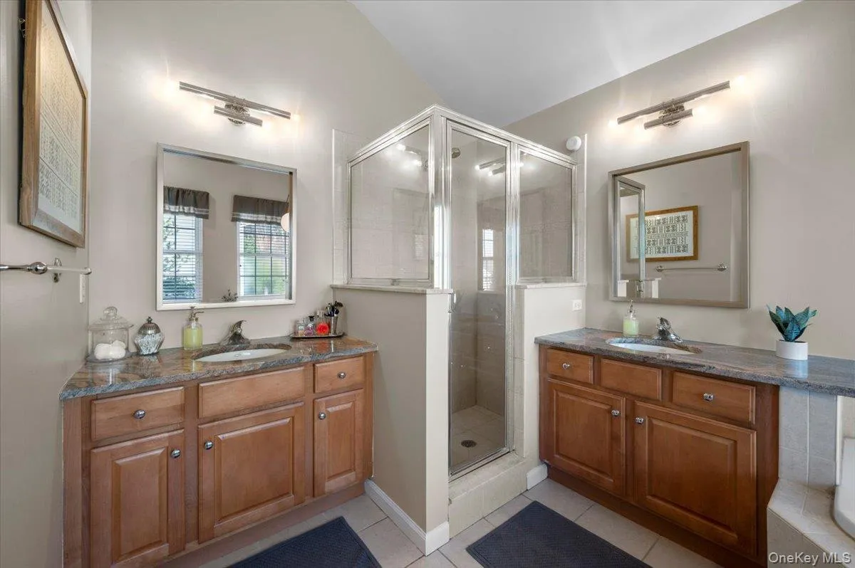 Bathroom featuring light tile patterned floors, a shower stall, and two vanities Bathroom featuring light tile patterned floors, a shower stall, and two vanities