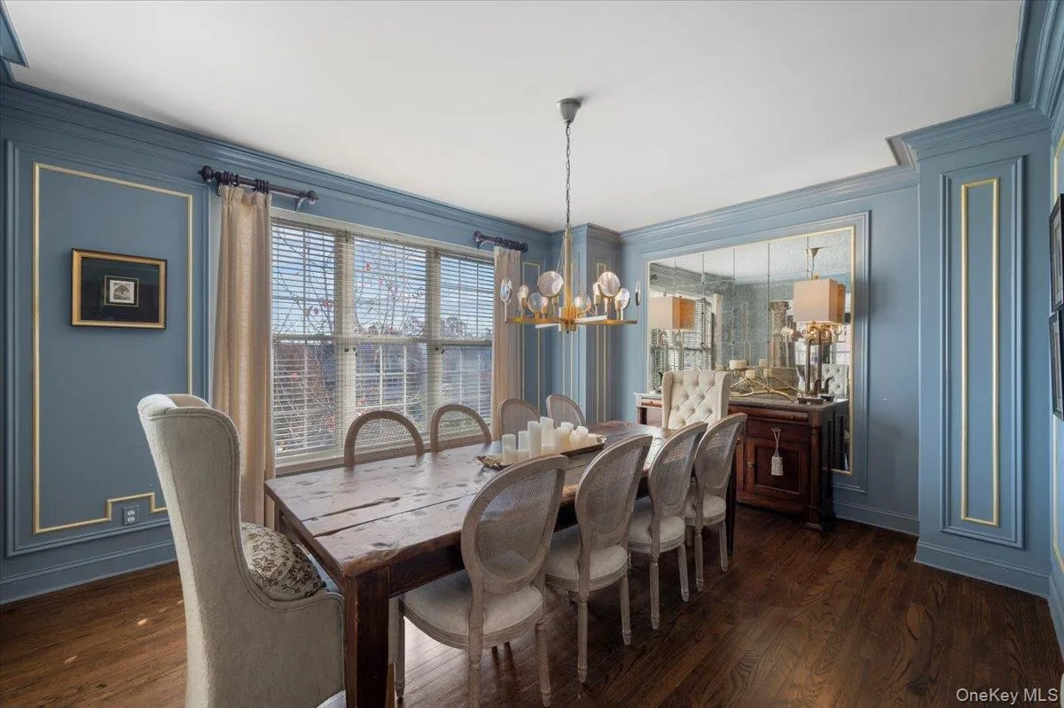 Dining area with a chandelier, dark wood-type flooring, crown molding, and a decorative wall Dining area with a chandelier, dark wood-type flooring, crown molding, and a decorative wall