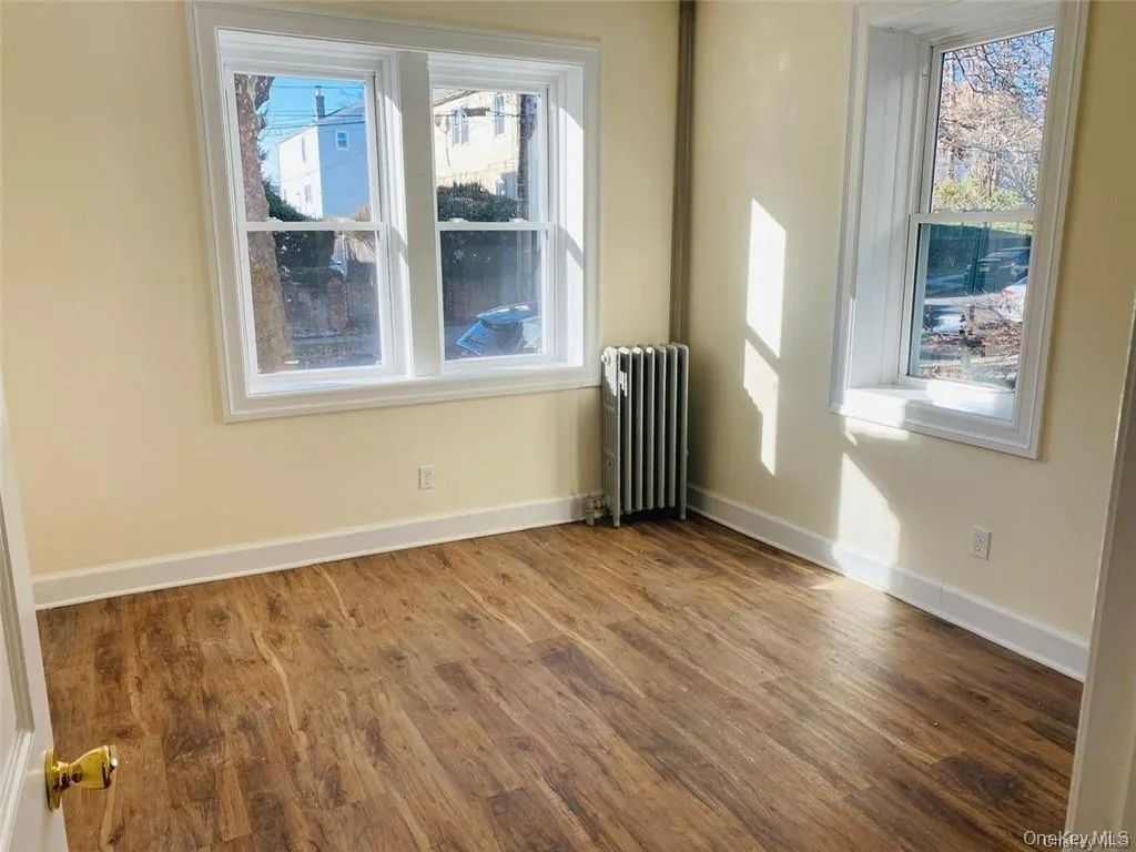 Unfurnished room with radiator heating unit, plenty of natural light, and wood finished floors Unfurnished room with radiator heating unit, plenty of natural light, and wood finished floors