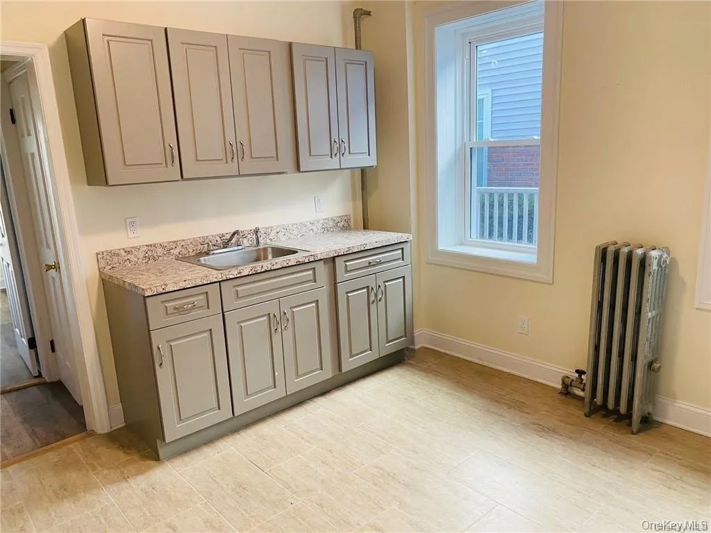 Kitchen featuring gray cabinetry, radiator, and light stone countertops Kitchen featuring gray cabinetry, radiator, and light stone countertops