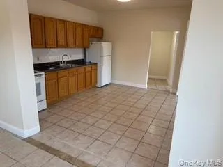 Kitchen with dark countertops, brown cabinetry, a sink, white appliances, and baseboards Kitchen with dark countertops, brown cabinetry, a sink, white appliances, and baseboards