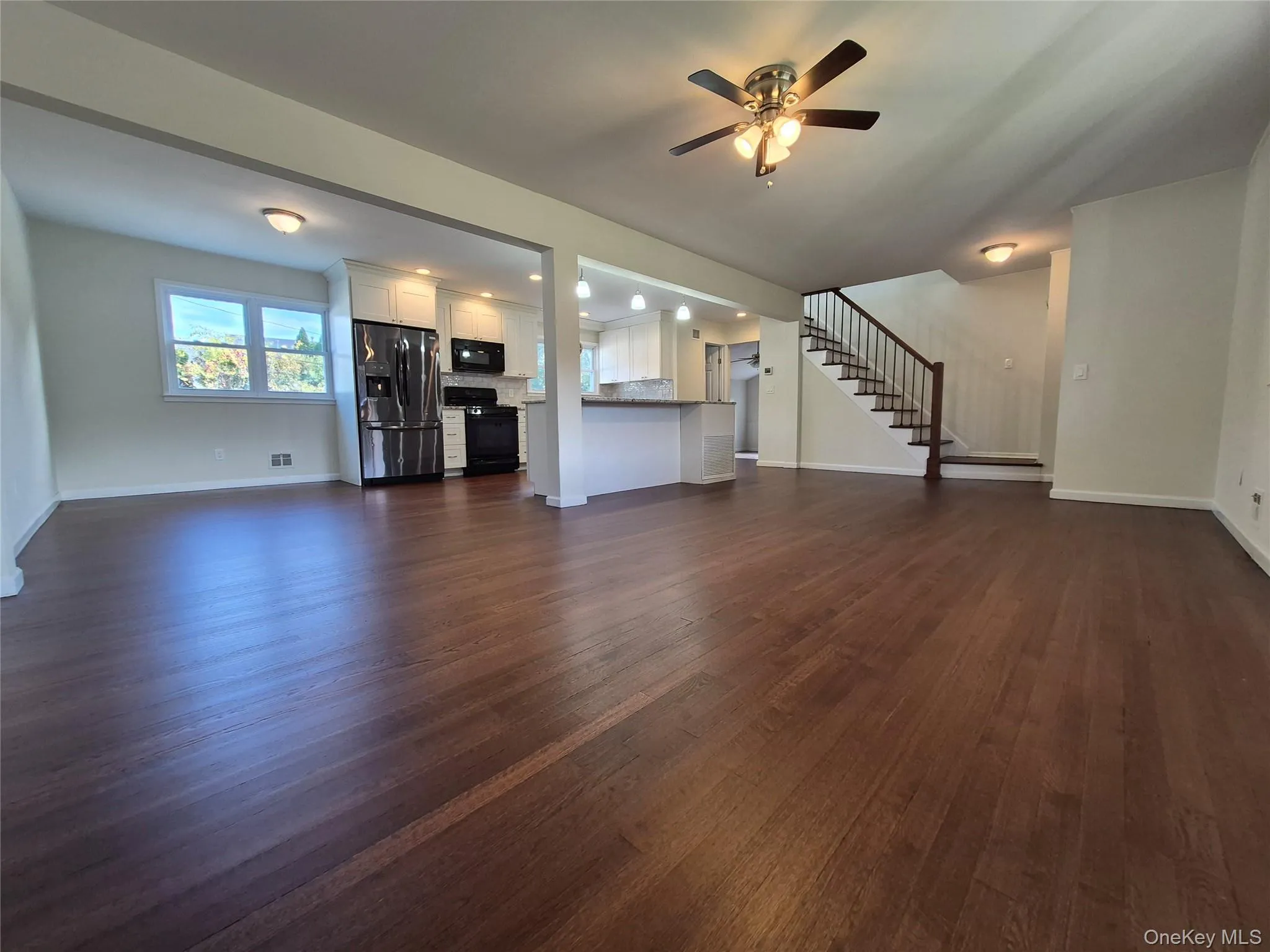 Unfurnished living room featuring stairs, dark wood finished floors, and a ceiling fan Unfurnished living room featuring stairs, dark wood finished floors, and a ceiling fan